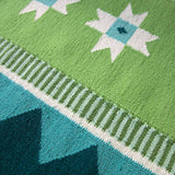 Detail of flatweave runner rug, handwoven from wool in vibrant shades of green with a geometric design inspired by Victorian tiles.